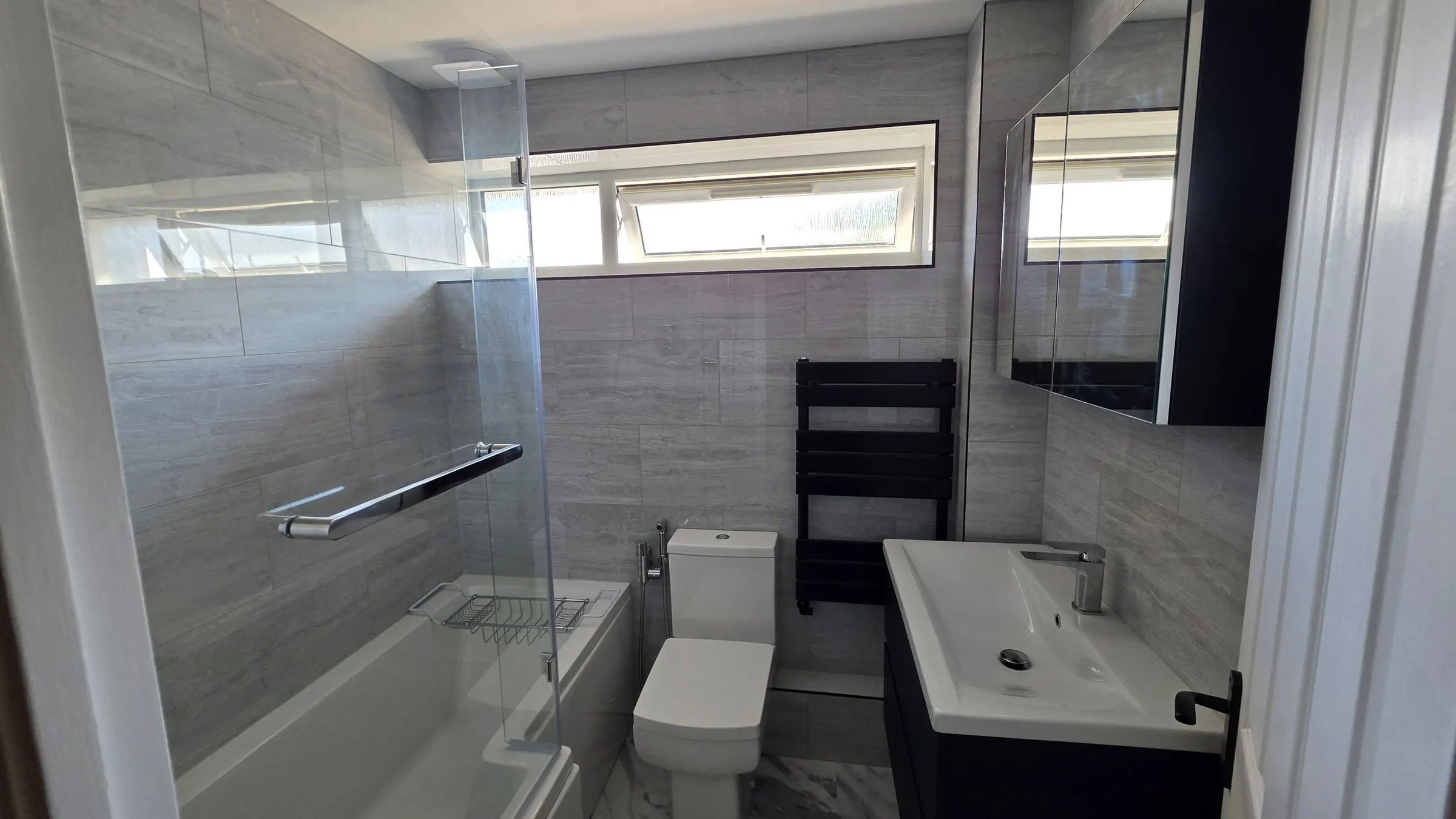 Finished bathroom refit by RefurbFerg: grey tiles, glass bath screen and black towel radiator
